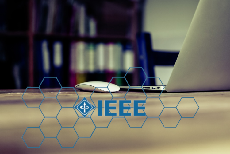 Grafika z logo IEEE i komputerem na stole - dotyczy sympozjum 